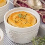 Individual freezer-friendly chicken and gravy casseroles baked in white ramekins with golden biscuit tops, garnished with parsley and fresh thyme.