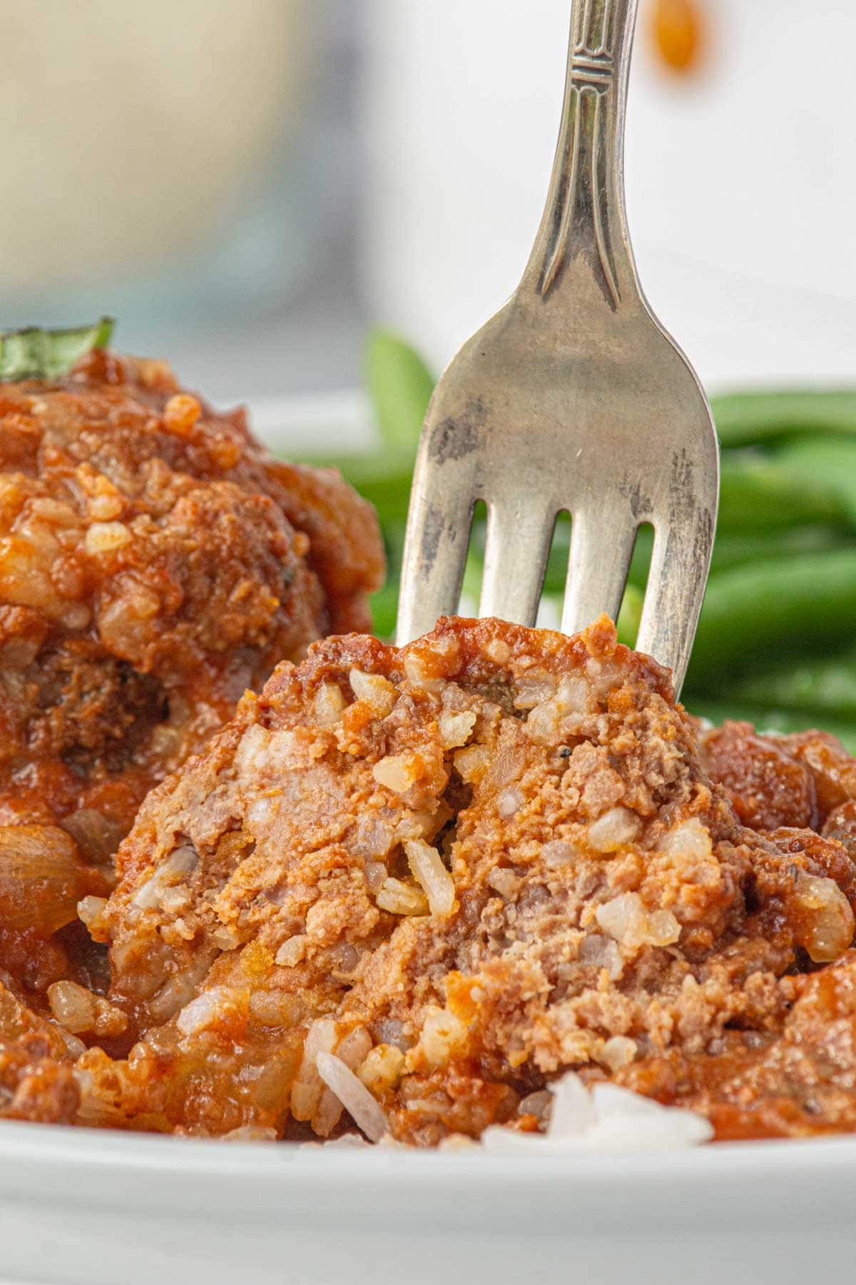 A fork cutting into tender porcupine meatballs with tomato soup sauce.