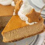 Slice of gingerbread cheesecake being lifted from the whole cake, topped with whipped cream and a star-shaped gingerbread cookie.