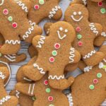 Christmas gingerbread cut out cookies decorated with white icing and red and green buttons, stacked on a wooden background.