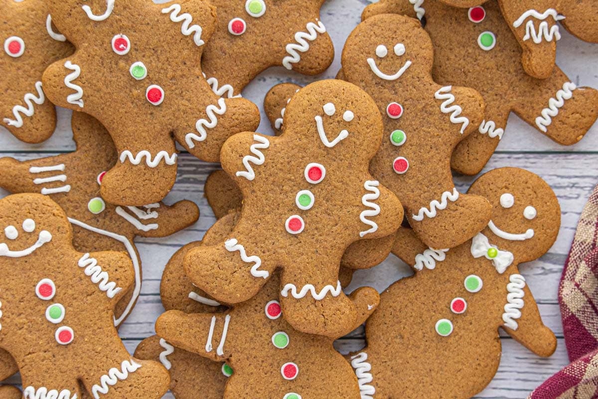 Christmas gingerbread cut out cookies decorated with white icing and red and green buttons, stacked on a wooden background.