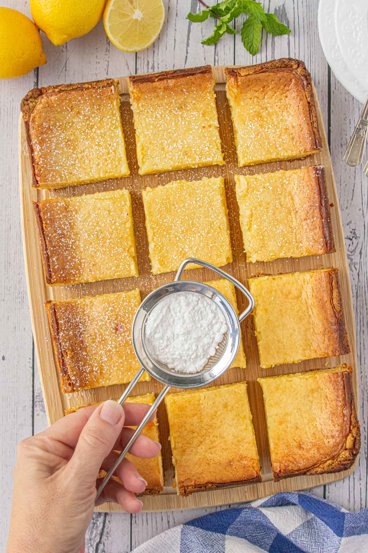 Baked lemon chess bars cut on a board being sprinkled with powdered sugar.