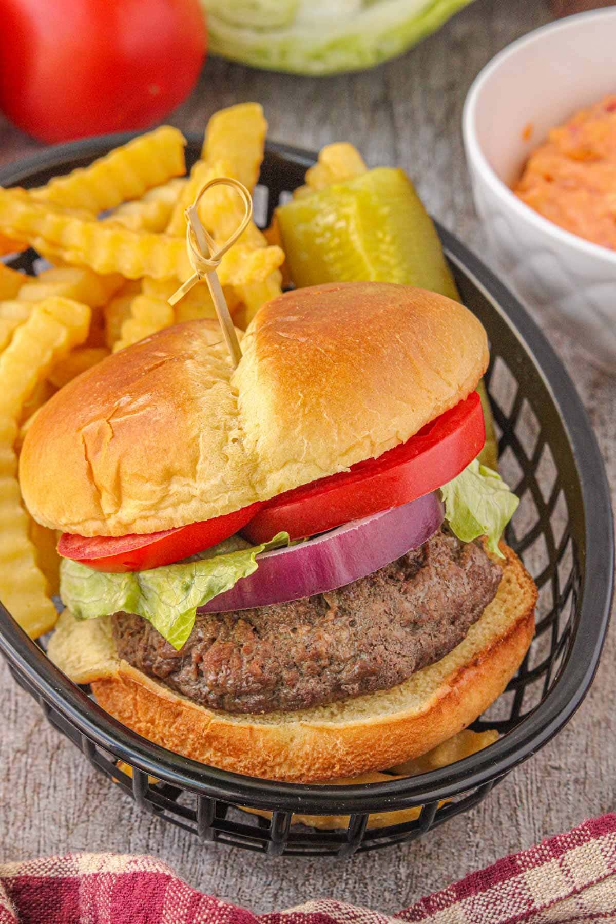 Pimento stuffed burger on a bun with onion, tomato and lettuce shown in a basket with crinkle cut fries.
