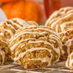 Pumpkin oatmeal cookies with icing drizzle cooling on a wire rack, with small pumpkins in the background for a fall touch.