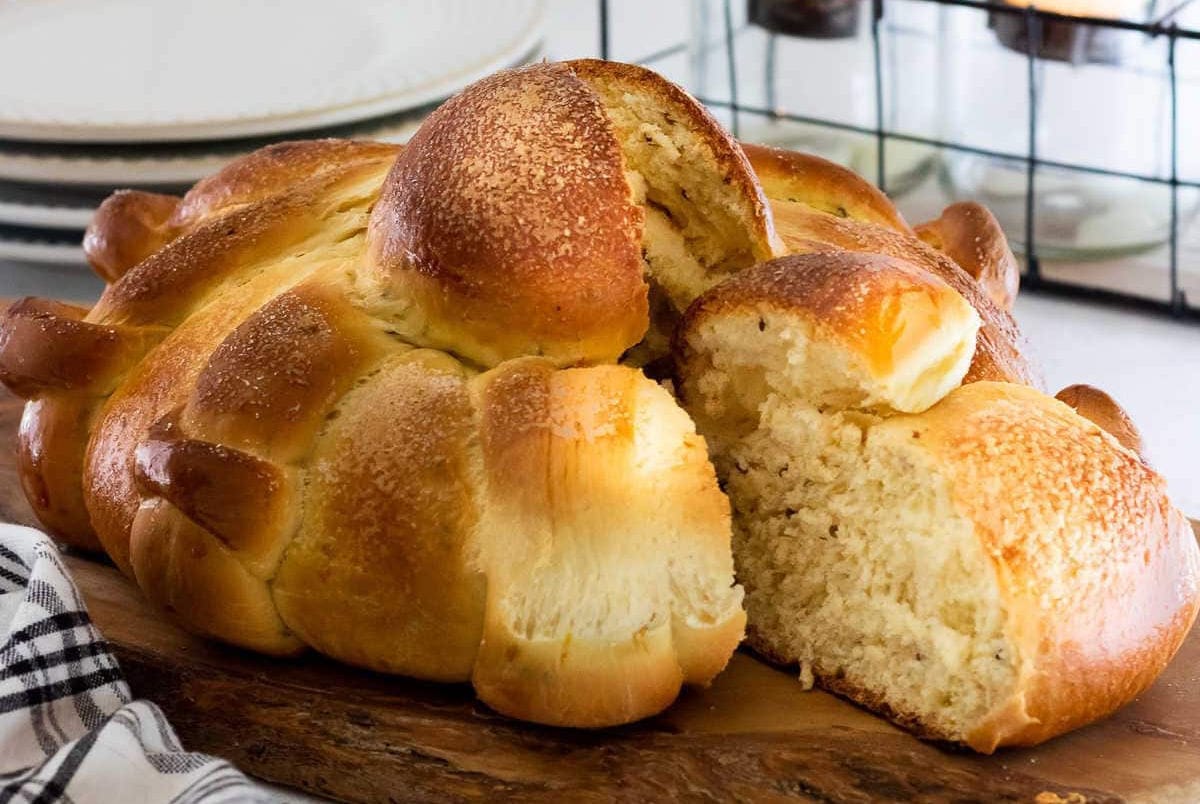 Freshly baked Pan de Muerto loaf cut open to show the soft, fluffy crumb inside, topped with sugar and decorated with bone-shaped dough pieces.