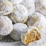 Plate of powdered sugar-covered nut-free gingerbread snowball cookies, one with a bite revealing a soft, spicy center.