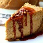 A slice of New York style pumpkin cheesecake with a gingersnap crust drizzled with bourbon caramel syrup and sprinkled with toasted pecans.