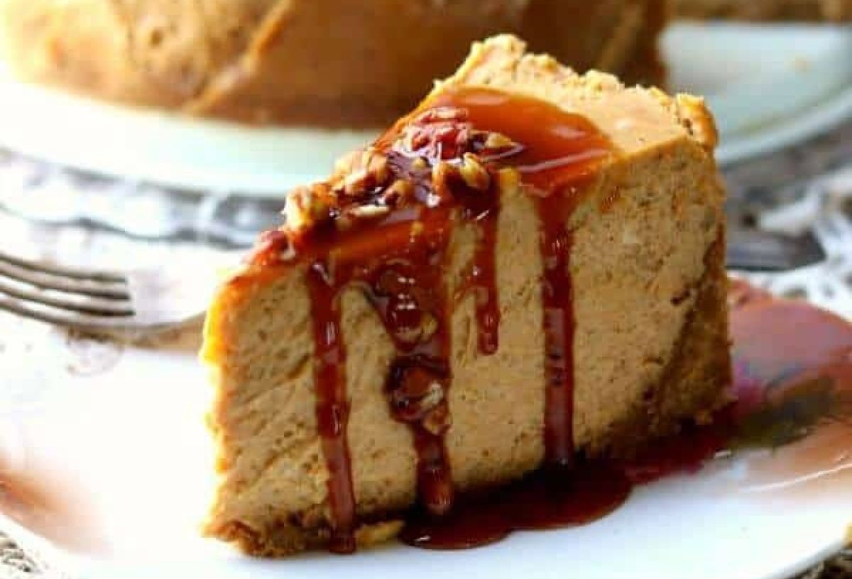 A slice of New York style pumpkin cheesecake with a gingersnap crust drizzled with bourbon caramel syrup and sprinkled with toasted pecans.