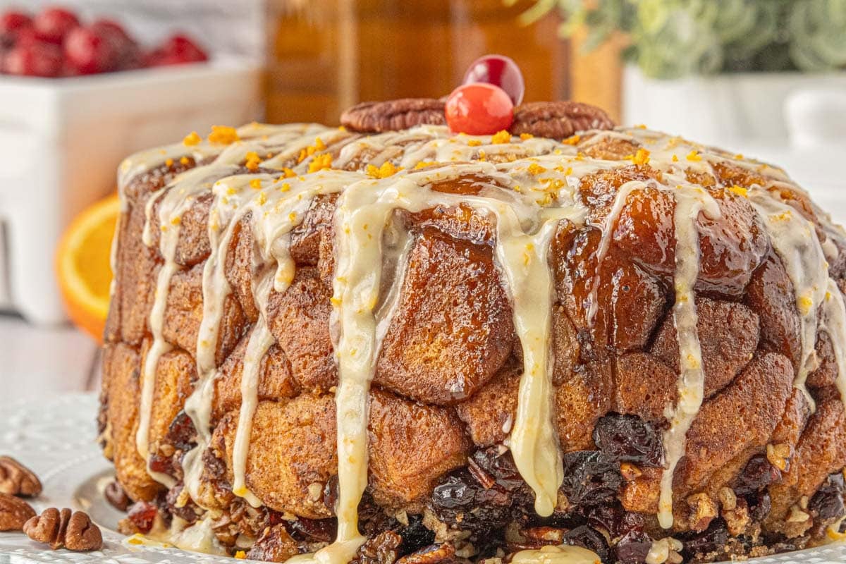 A loaf of slow cooker monkey bread with pecans and cranberries covered in orange glaze on a plate.