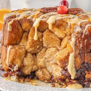 Close-up of crockpot monkey bread drizzled with orange glaze and topped with pecans and cranberries — soft pull-apart cinnamon bread perfect for Christmas morning.
