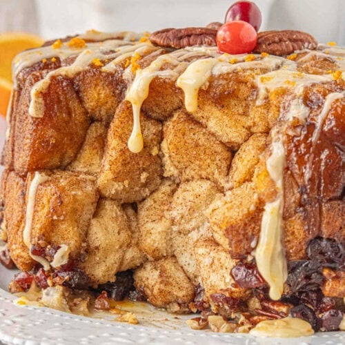Close-up of crockpot monkey bread drizzled with orange glaze and topped with pecans and cranberries - soft pull-apart cinnamon bread perfect for Christmas morning.