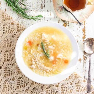 Overhead view of chicken and rice soup with ginger in a white bowl on a chippy white farmhouse table.