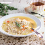 Easy on the stomach ginger chicken and rice soup in a white bowl on a lace tablecloth.