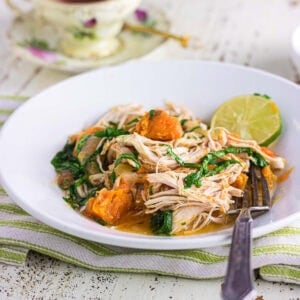 Closeup of chicken and sweet potato stew in a white bowl with a fork in it.