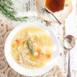 A bowl of ginger chicken and rice soup on a chippy farmhouse table with a cup of tea next to it. Text overlay for Pinterest "Ginger Chicken and Rice Soup" "Light and easy on the digestive system for chemo patients"
