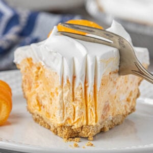 A thick slice of orange Tang pie with Cool Whip on top and mandarin orange garnish, sitting on a white plate as a fork presses into it.