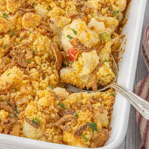 Golden baked cauliflower casserole with bell peppers and cornbread topping, served in a white dish with a vintage spoon.