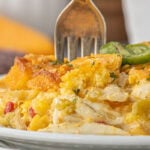 Close-up of a serving of cheesy chicken and chile cornbread casserole on a white plate, showing the golden cornbread topping, tender shredded chicken, diced chiles, and sliced jalapeños.