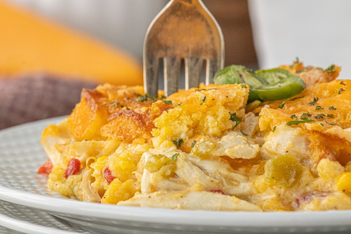 Close-up of a serving of cheesy chicken and chile cornbread casserole on a white plate, showing the golden cornbread topping, tender shredded chicken, diced chiles, and sliced jalapeños.