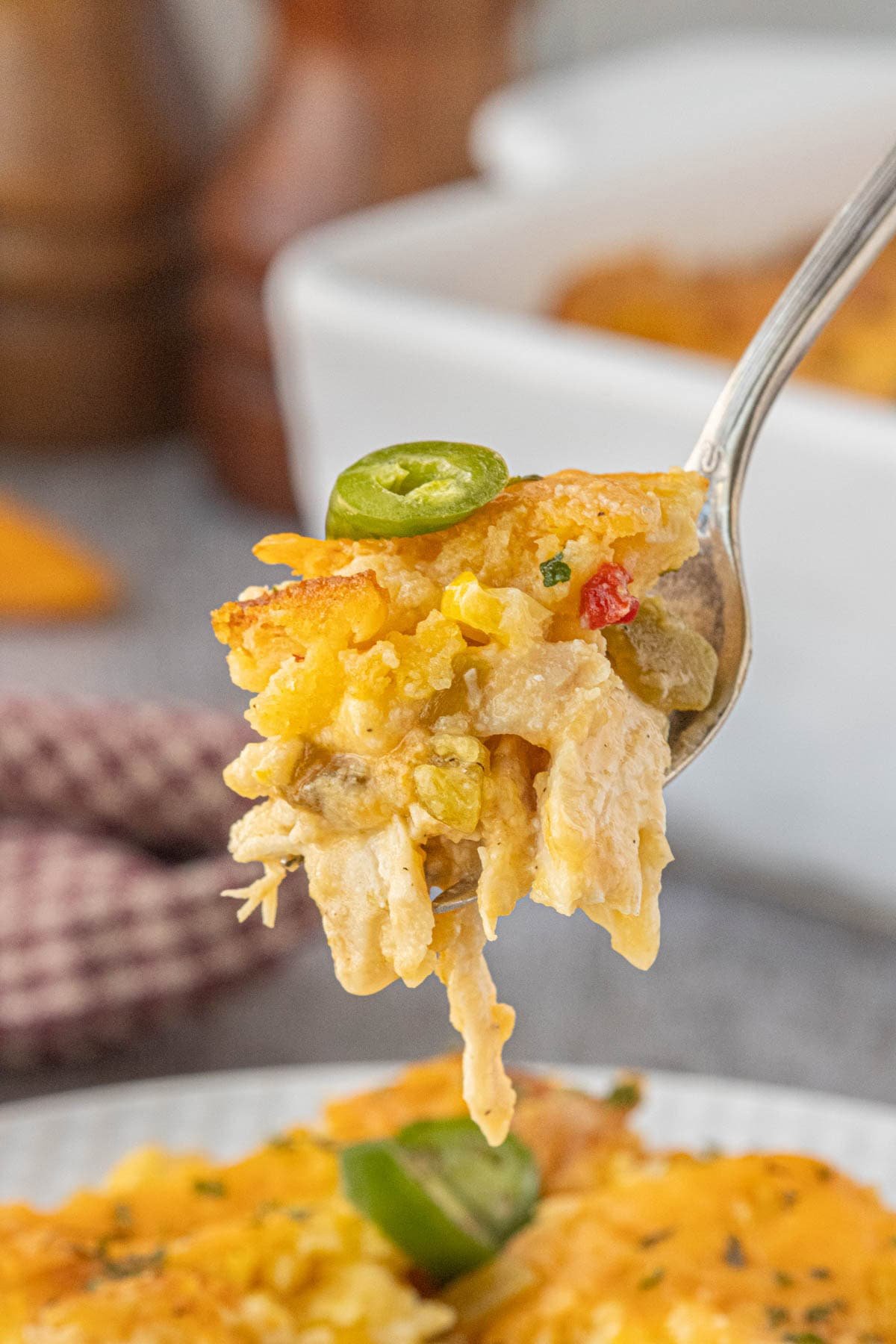 A close-up spoonful of cheesy chicken and chile cornbread casserole, showing tender shredded chicken, corn, peppers, and a golden cornbread topping with a slice of jalapeño.