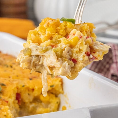 A close-up spoonful of cheesy chicken and chile cornbread casserole lifted from the baking dish, showing the golden cornbread topping, tender shredded chicken, diced chiles, and creamy filling.