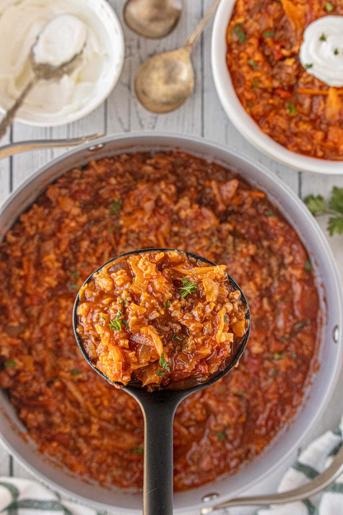 A close-up of a ladle scooping cabbage roll soup, showing tender cabbage pieces, ground beef, and rice coated in a glossy tomato sauce.
