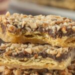 Close-up of browned butter saltine toffee pieces stacked together, showing the crisp cracker base, glossy chocolate layer, and chopped nut topping with a rich caramel sheen.