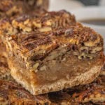 Extreme close-up of stacked brown butter pecan pie bars, emphasizing the glossy pecan topping, gooey brown butter filling, and crumbly shortbread base.