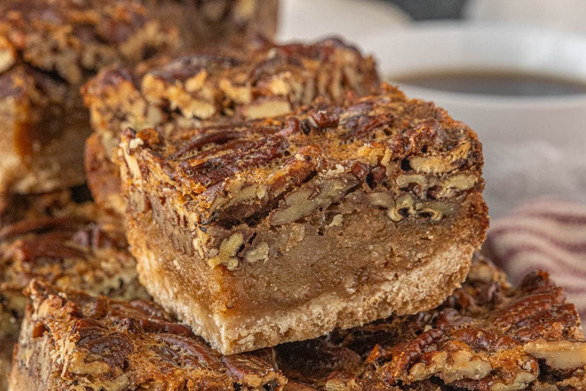 Extreme close-up of stacked brown butter pecan pie bars, emphasizing the glossy pecan topping, gooey brown butter filling, and crumbly shortbread base.