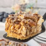 Gooey sweet cinnamon roll breakfast casserole being served from a white casserole dish.