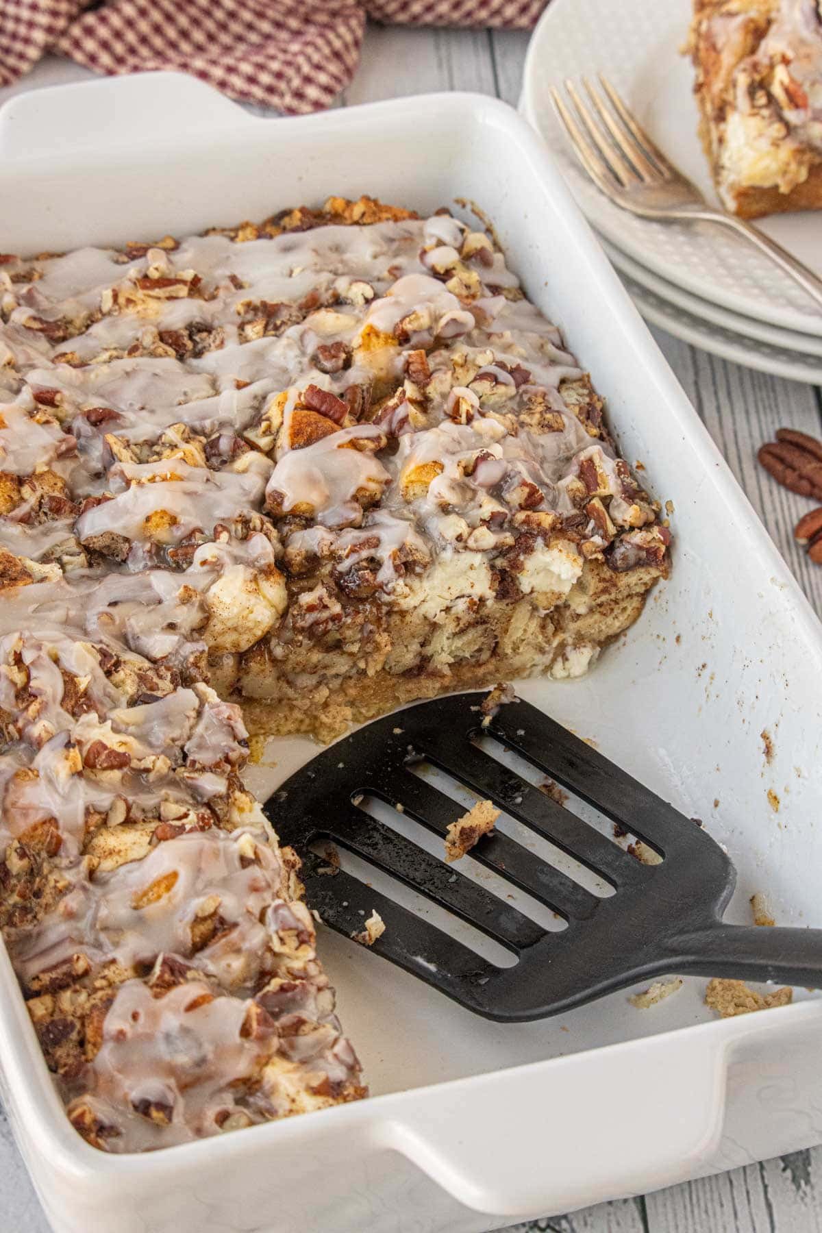 Baking dish of cinnamon roll breakfast casserole with a missing piece, showing the gooey cinnamon center and crunchy pecan topping