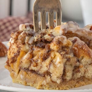Square of cinnamon roll breakfast casserole lifted from the pan on a spatula, revealing the soft custardy layers, cinnamon swirls, and thick icing on top.