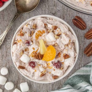 Close-up bowl of cranberry ambrosia salad with mandarin oranges, pineapple, cranberries, pecans, and mini marshmallows mixed into pink whipped cream.