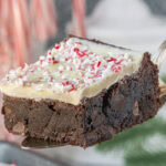 Peppermint bark brownie on spatula with candy canes in the background, showcasing fudgy chocolate layer and crushed peppermint topping.