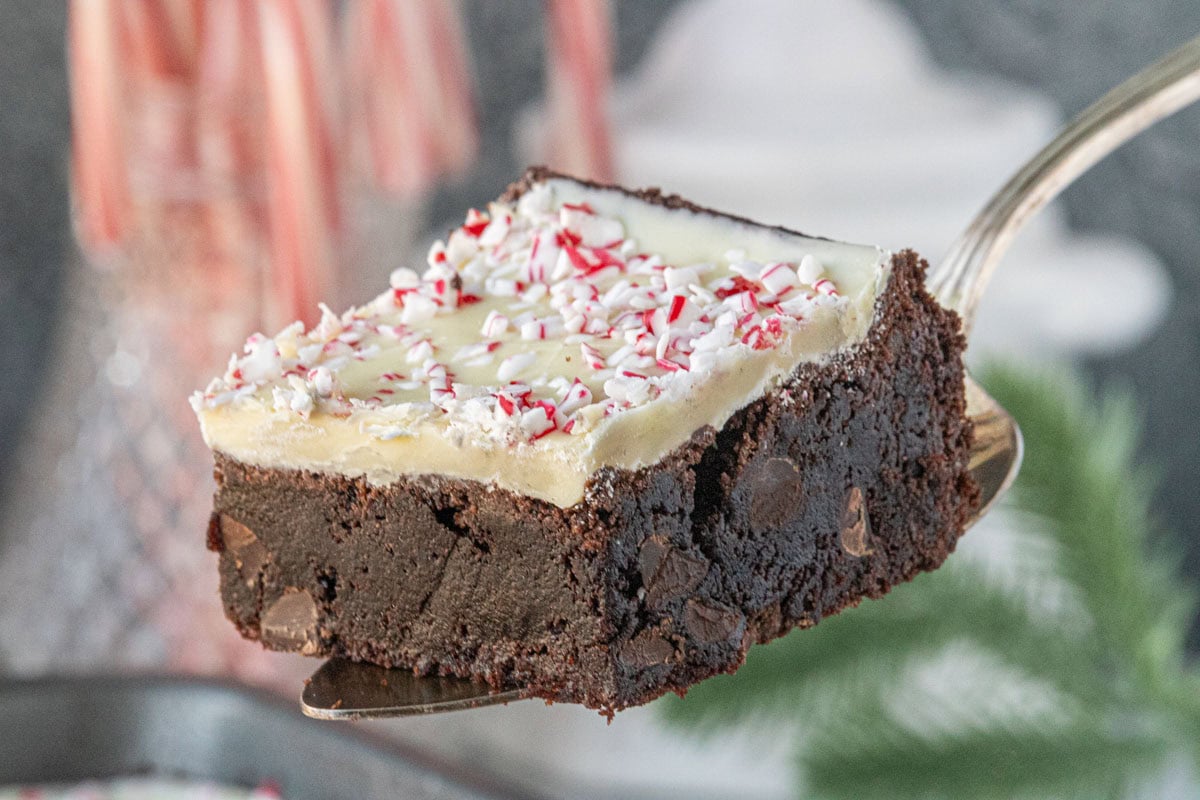 Peppermint bark brownie on spatula with candy canes in the background, showcasing fudgy chocolate layer and crushed peppermint topping.