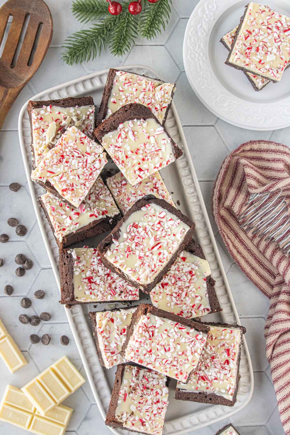 Overhead view of a platter stacked with peppermint bark brownies topped with white chocolate and crushed candy canes, ready for holiday serving.