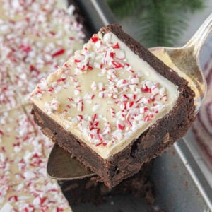 Thick peppermint bark brownie lifted from pan with fudgy chocolate base, white chocolate topping, and crushed peppermint pieces.