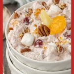 Tall Pinterest graphic showing a bowl of cranberry ambrosia salad topped with mandarin oranges, pineapple, pecans, and marshmallows, with text that reads “Cranberry Ambrosia Salad — Grandma approved. Probably.”