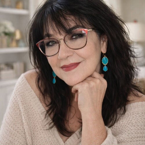 Marye Audet-White smiling in her kitchen, wearing glasses and turquoise earrings
