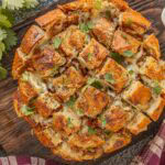 Bacon ranch pull-apart bread baked in a round loaf, golden and crispy on top with melted cheese and chopped cilantro scattered over the surface.