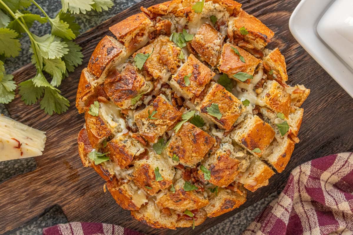 Bacon ranch pull-apart bread baked in a round loaf, golden and crispy on top with melted cheese and chopped cilantro scattered over the surface.