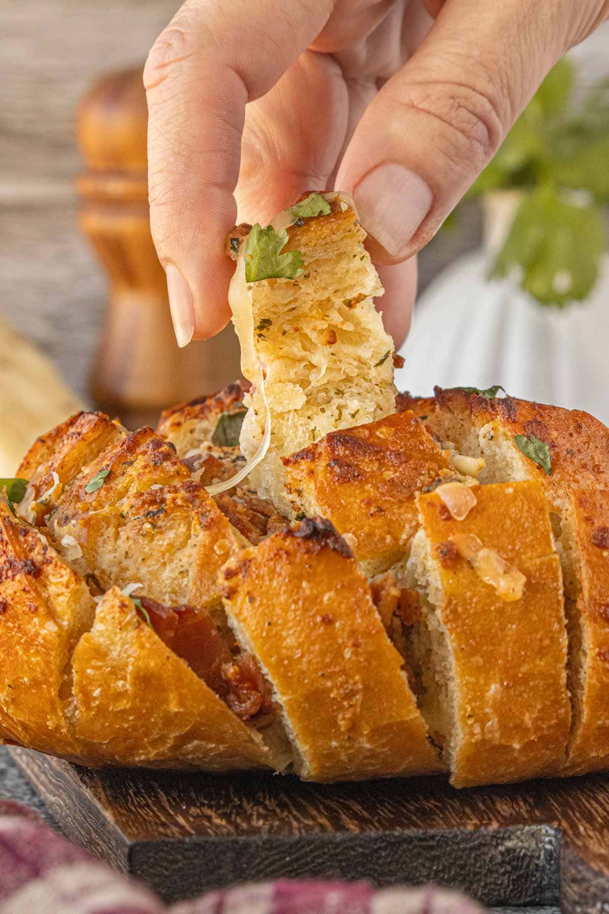 Hand pulling a cheesy piece from bacon ranch pull-apart bread, showing soft interior crumb, melted cheese stretch, and crisp golden crust.