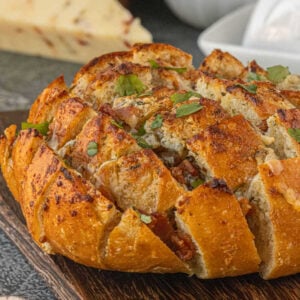 Bacon ranch pull-apart bread baked in a round loaf, golden and crispy on top with melted cheese and chopped cilantro scattered over the surface.