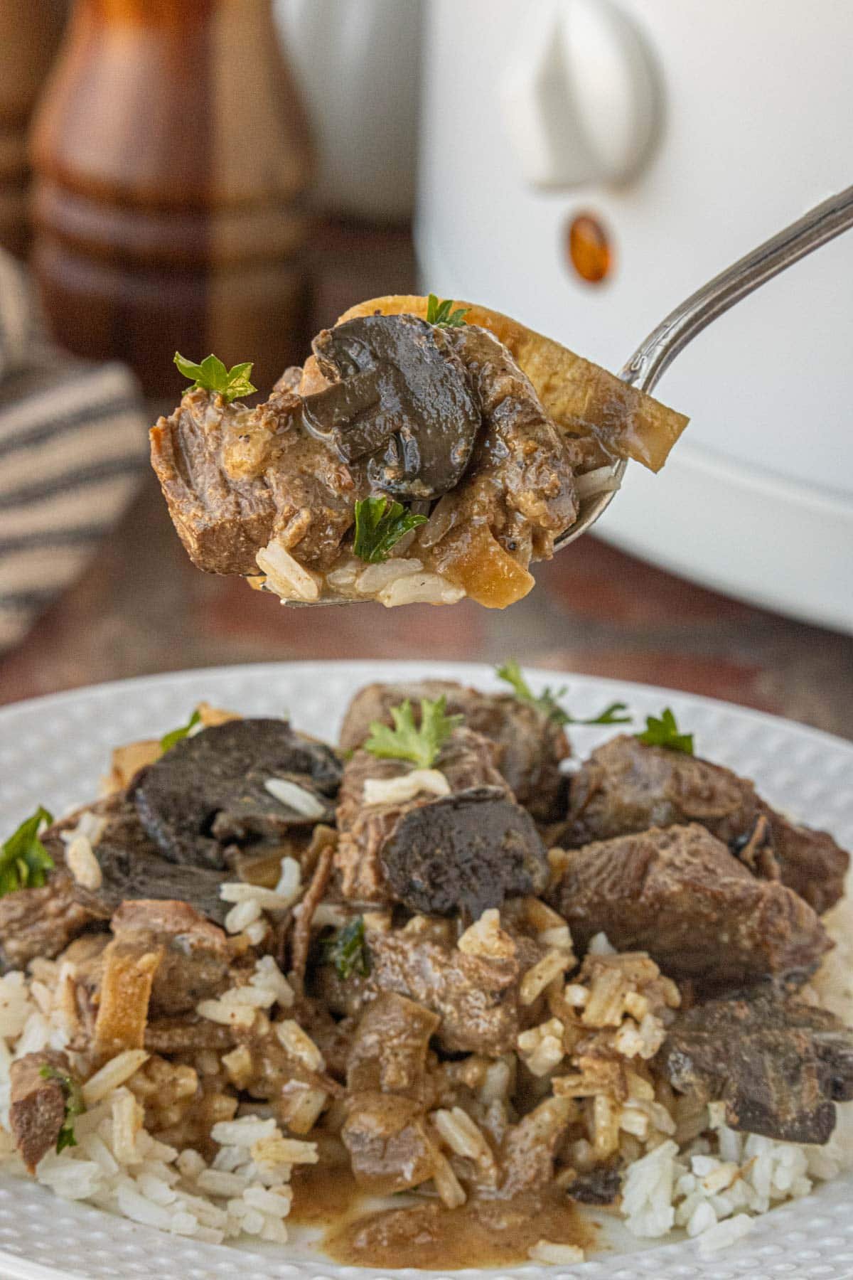 Spoonful of slow cooker beef tips with mushrooms and gravy over rice, tender and savory