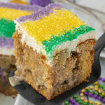King Cake Poke Cake being served on a black spatula.