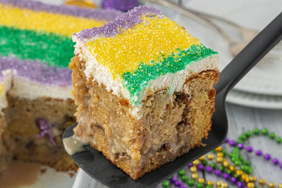 King Cake Poke Cake being served on a black spatula.
