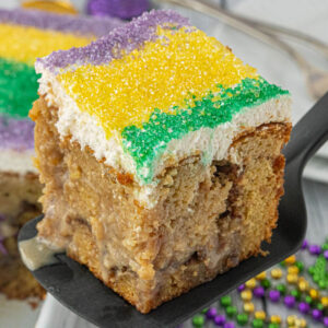 Close-up of king cake poke cake slice with cinnamon swirl layers and cream cheese frosting topped with purple, green, and gold sugar