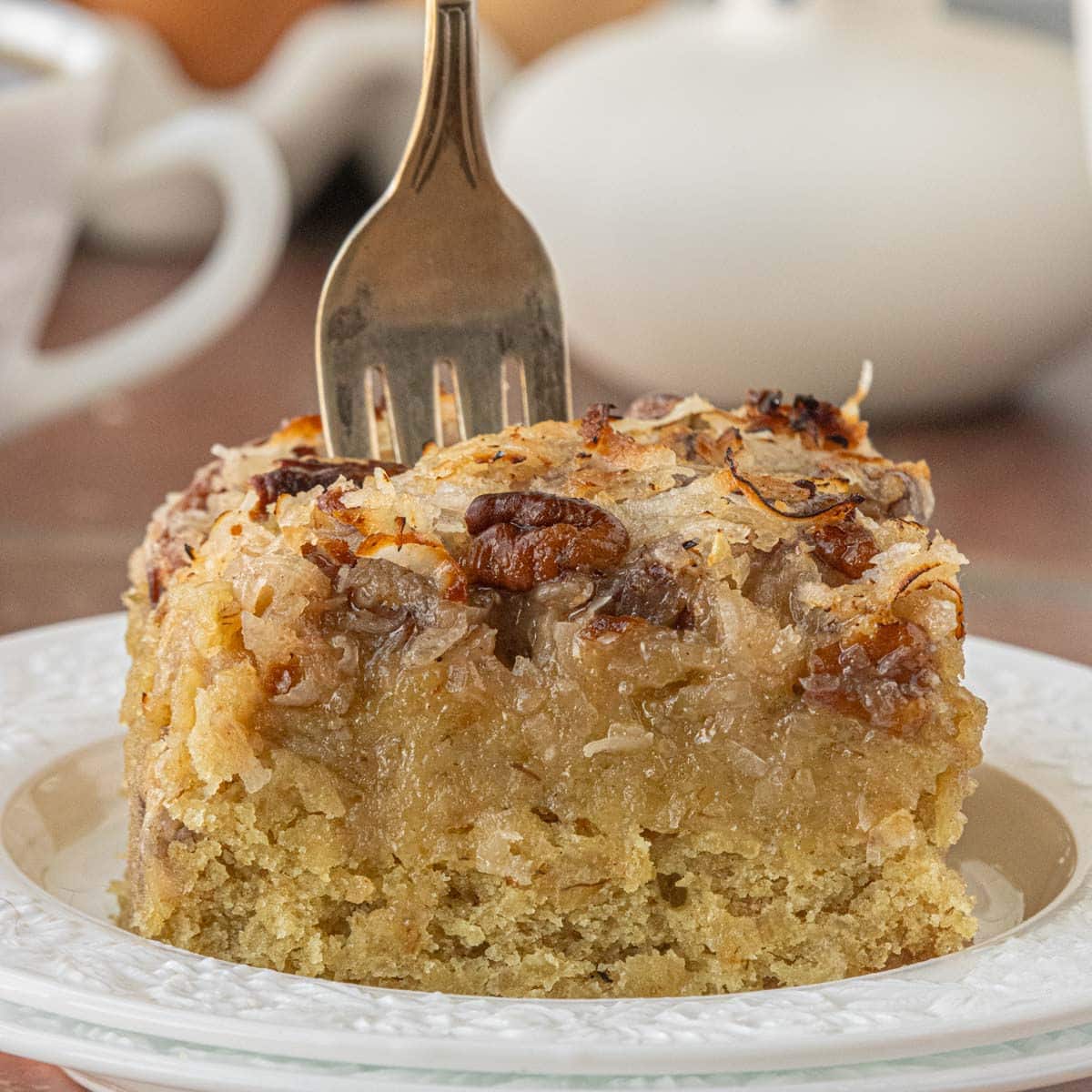Slice of old-fashioned oatmeal cake with coconut pecan topping on a white plate with a fork