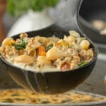 Ladle of creamy Italian sausage and cannellini bean soup with sausage, white beans, carrots, and greens held over a pot of simmering soup, photographed by Kim Ledet for Marye at Restless Chipotle.
