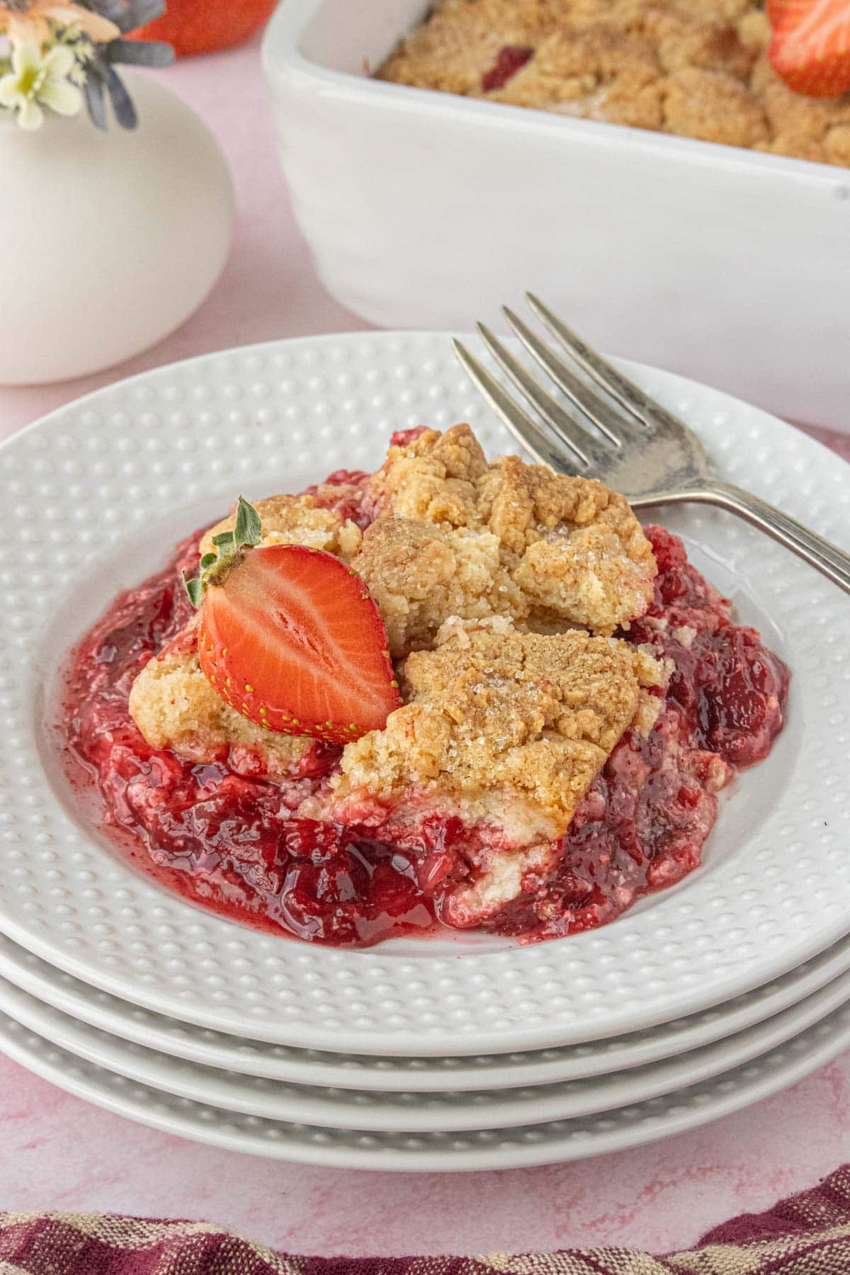 Plated strawberry cream cheese dump cake with crumb topping and fresh strawberry garnish on a white dessert plate